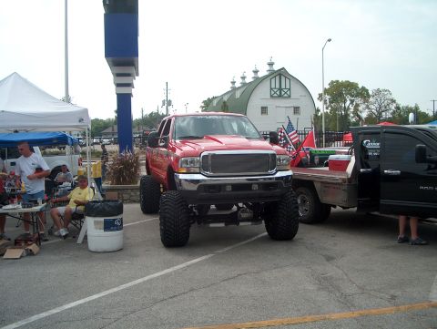 1978 Ford Bronco - Lifted red pickup truck parked next to a black truck with flags in the bed.
