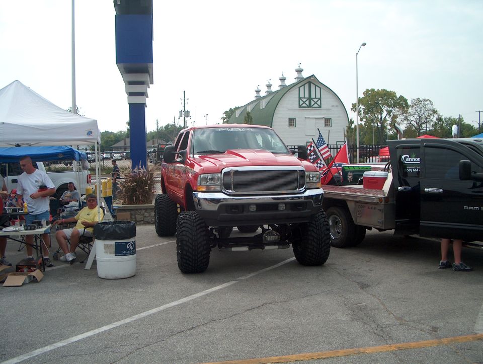Lifted red pickup truck with large tires parked next to a black truck. American and Confederate flags are on the truck bed