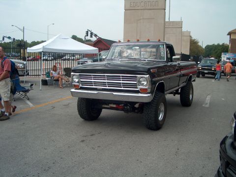 1978 Ford Bronco - A lifted black pickup truck is parked on a street with a large building in the background.