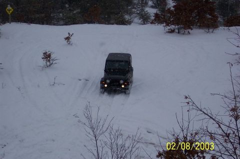 1978 Ford Bronco - A black Jeep Wrangler navigates a snowy terrain, leaving tire tracks in the fresh snow.