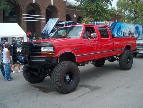1978 Ford Bronco - This lifted red pickup truck features a prominent aftermarket grille and oversized tires, suggesting a model from the mid-1990s.