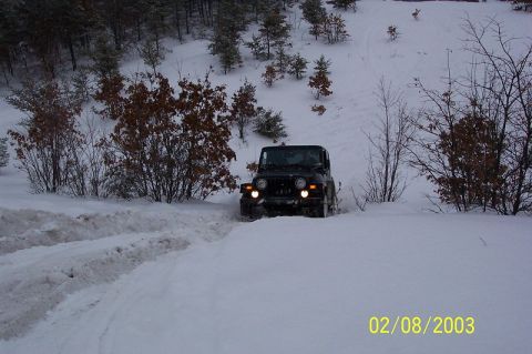 1978 Ford Bronco - Jeep Wrangler navigates a snow-covered path with trees in the background.