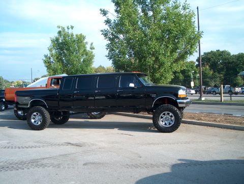 1978 Ford Bronco - A heavily modified black pickup truck, stretched into a limousine, sits parked on a paved surface.