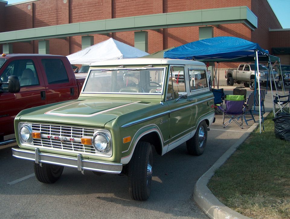 Green 1978 Ford Bronco parked next to a red pickup truck, with tents and chairs in the background