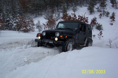 1978 Ford Bronco - A black Jeep Wrangler navigates a snow-covered path in a wooded area.