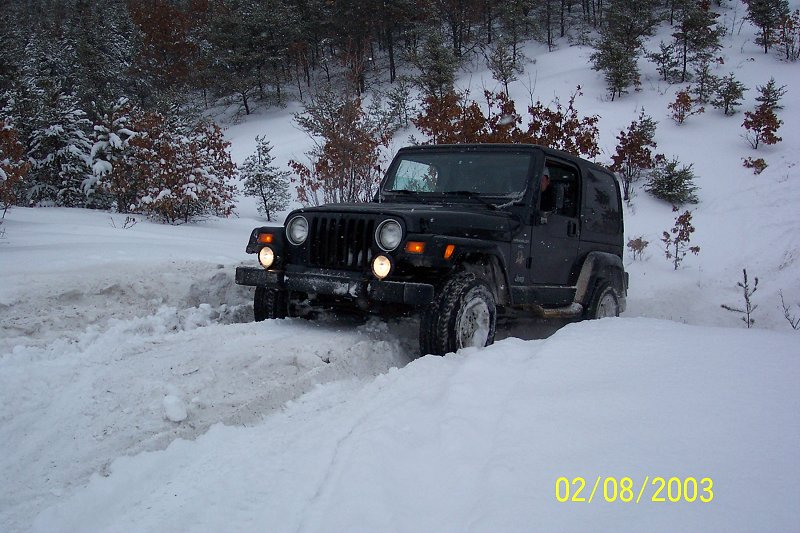 Black Jeep Wrangler driving through snow, front quarter view