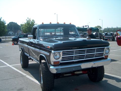 1978 Ford Bronco - This lifted black pickup truck features a prominent chrome grille, suggesting a 1970s model year. Multiple vehicles are visible in the back…