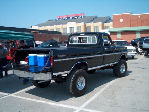 1978 Ford Bronco - Lifted black Ford pickup truck parked at an outdoor event with other vehicles present.