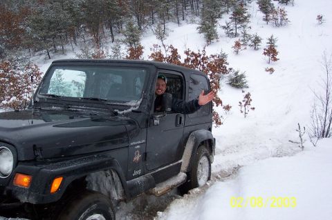 1978 Ford Bronco - A black Jeep Wrangler navigates a snowy trail with a driver visible through the window.