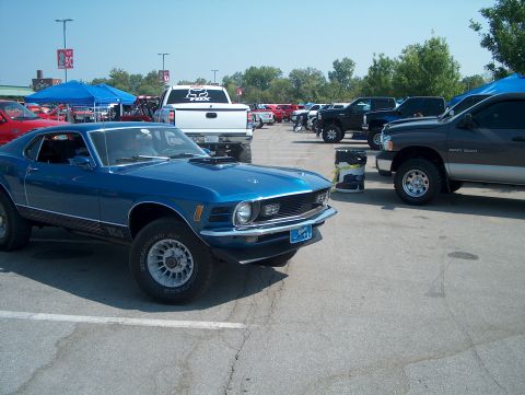 1978 Ford Bronco - A blue 1970 Ford Mustang Mach 1 is parked in a lot with other vehicles and tents in the background.