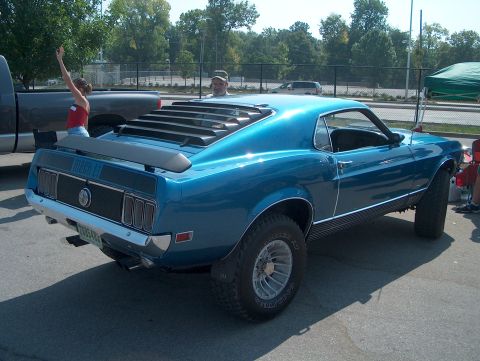 1978 Ford Bronco - A modified 1969 Ford Mustang Mach 1 is shown from the rear, parked outdoors with a lifted pickup truck nearby.