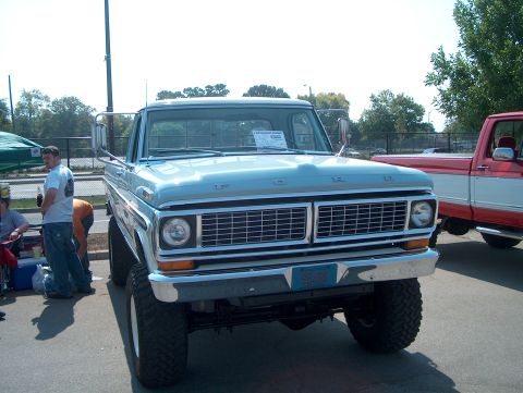1978 Ford Bronco - A light blue Ford F-Series truck is shown from the front, lifted with large tires, with a red truck to its right.