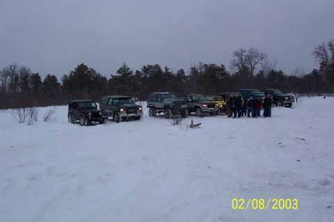 1978 Ford Bronco - A group of off-road vehicles are gathered in a snow-covered landscape under an overcast sky.