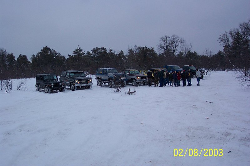 Several SUVs and trucks parked in a snowy field with trees in the background