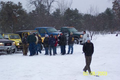 1978 Ford Bronco - Several vehicles and people are gathered in a snowy outdoor scene, with snowfall occurring.