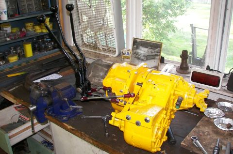 1988 Ford Bronco - A yellow transfer case with dual levers sits on a workbench, accompanied by tools and a vintage car photograph.