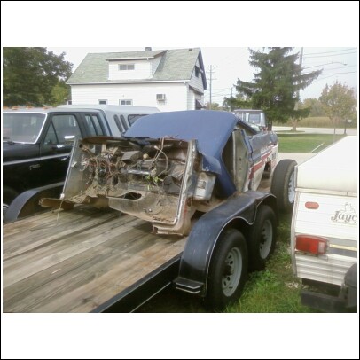 1977 Ford F-150 - The front section of a truck, stripped down to its frame and wiring, is transported on a trailer.