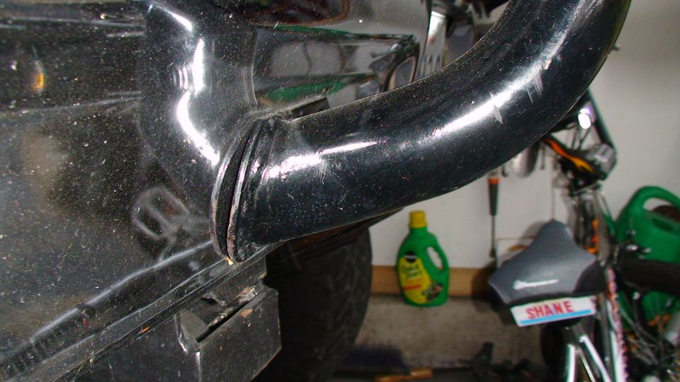 Black metal pipe attached to fender, with a bottle of cleaner and a seat in the background