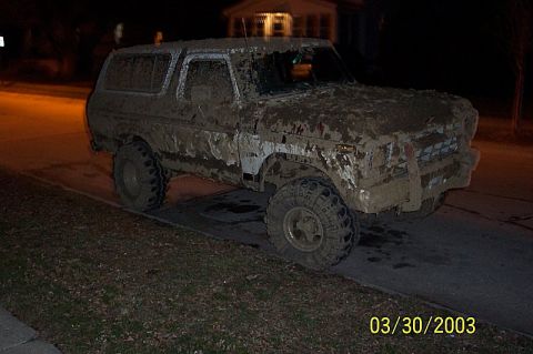 1978 Ford Bronco - A heavily mud-caked 1978 Ford Bronco sits on the side of a road at night, its body obscured by dirt.