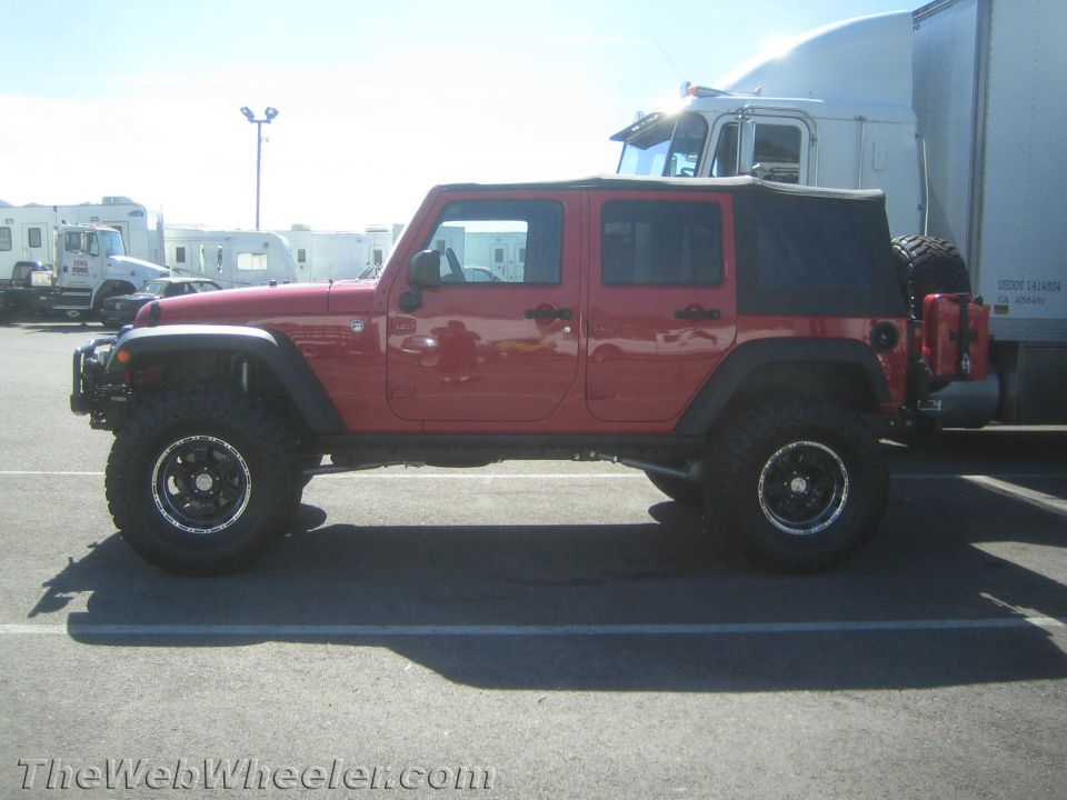 Red Jeep Wrangler with black soft top and off-road tires, parked in a lot