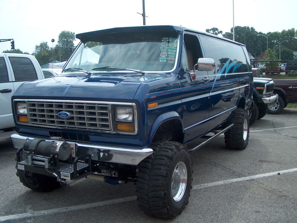 Dark blue lifted Ford Econoline van with big tires and front winch, 3/4 front view
