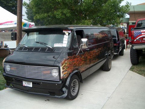 1978 Ford Bronco - A black van with flame decals is parked next to other vehicles.