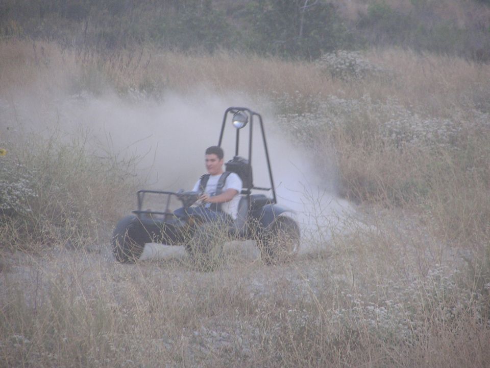 Young man driving an off-road go-kart buggy through dusty brush