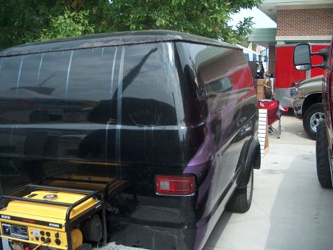1978 Ford Bronco - A black van with purple graphics is seen from the rear, parked next to a yellow generator and other vehicles.