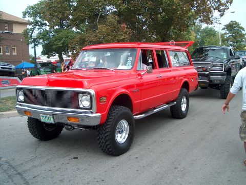 1978 Ford Bronco - A lifted red Chevrolet Suburban is seen in a procession with other vehicles.