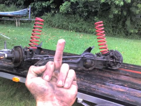 1995 Ford Bronco - A dirty hand gives the middle finger in front of a disassembled vehicle axle with bright red coil springs.