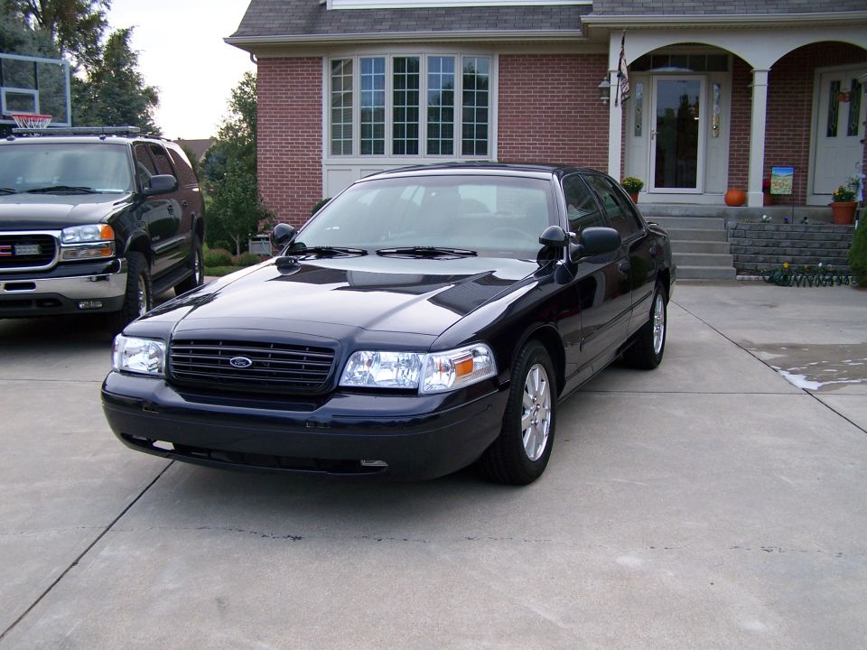 Black 2003 Ford Crown Victoria parked on driveway, GMC Yukon SUV in background