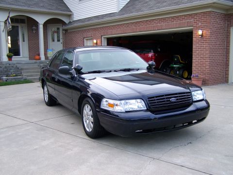 2003 Ford Crown Victoria - A dark blue Ford Crown Victoria police car is parked in front of a suburban home.