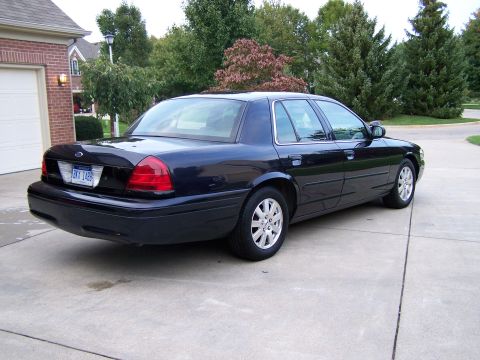 2003 Ford Crown Victoria - A dark blue 2003 Ford Crown Victoria sedan is parked on a concrete driveway in front of a house.