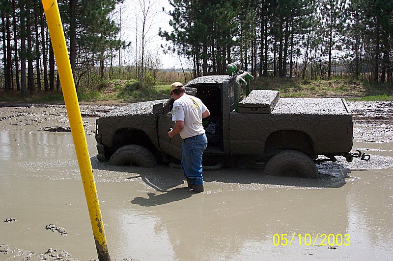 mud-covered pickup truck stuck in mud with a person standing next to it