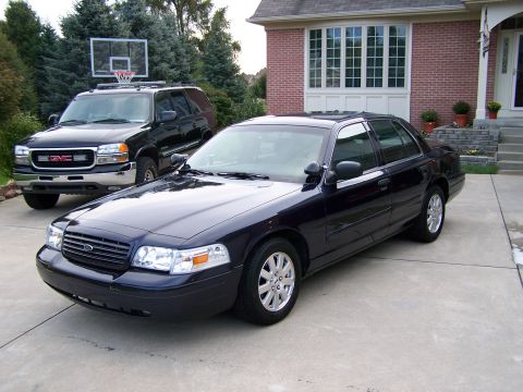 2003 Ford Crown Victoria - A dark blue 2003 Ford Crown Victoria sedan is parked in a driveway next to an SUV.