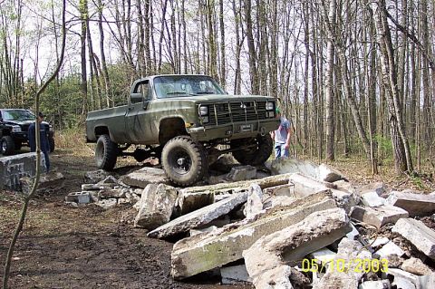 1978 Ford Bronco - A lifted olive green pickup truck navigates a challenging obstacle course in a wooded area.