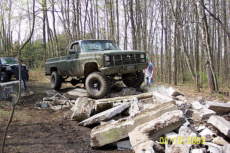 Olive green pickup truck with large tires on a rocky obstacle course