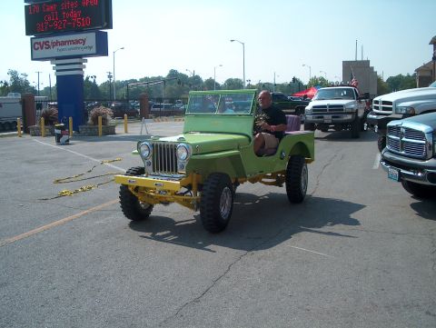 1978 Ford Bronco - A man drives a green jeep in a parking lot with other vehicles present.