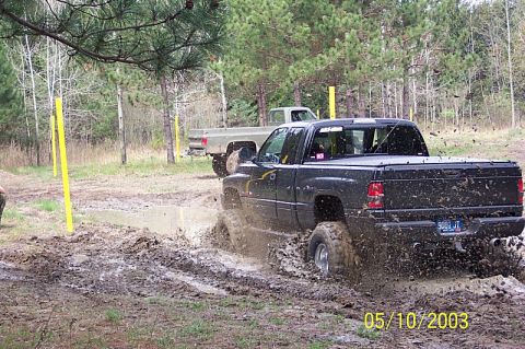 1978 Ford Bronco - Two trucks navigate a muddy off-road course, kicking up significant spray.