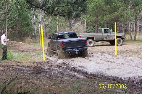 1978 Ford Bronco - Two trucks navigate a muddy off-road course with yellow poles marking the path.