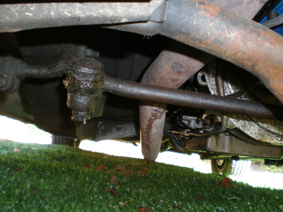 Underside view of a greasy steering linkage and exhaust pipe on a vehicle