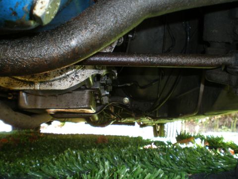 1966 Ford Mustang - The underside of a vehicle shows a transmission pan and oily mechanical parts.