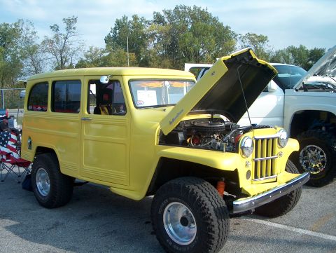 1978 Ford Bronco - A yellow woody wagon is parked with its hood open, revealing the engine, next to a white truck.