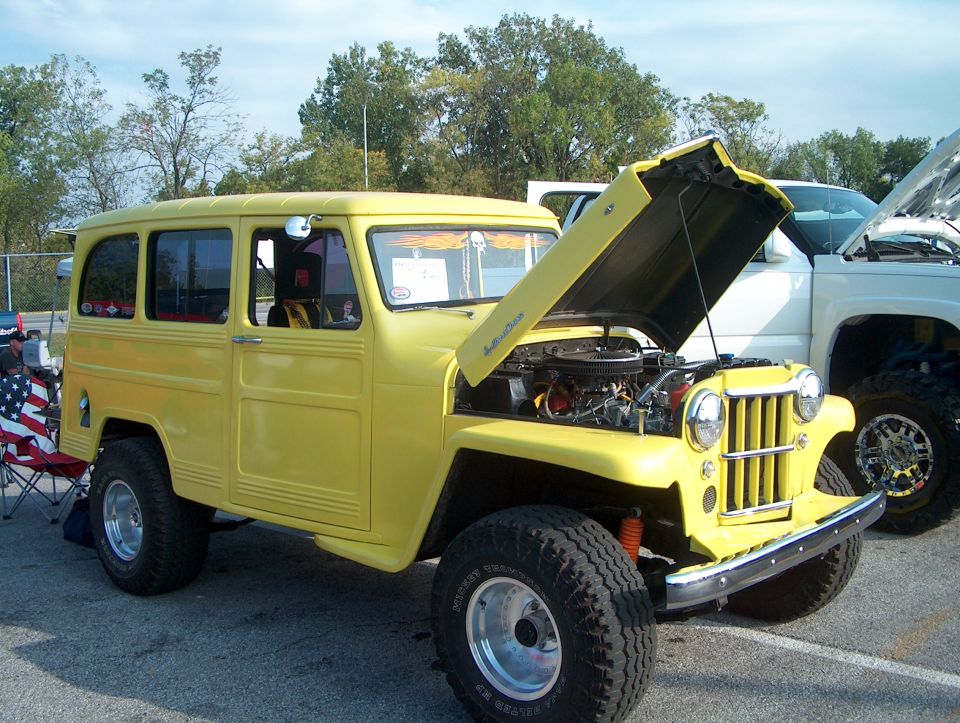 Yellow woody wagon with hood open, showing engine. Parked next to a white truck
