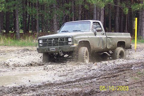 1978 Ford Bronco - A pickup truck navigates a muddy off-road course with trees in the background.