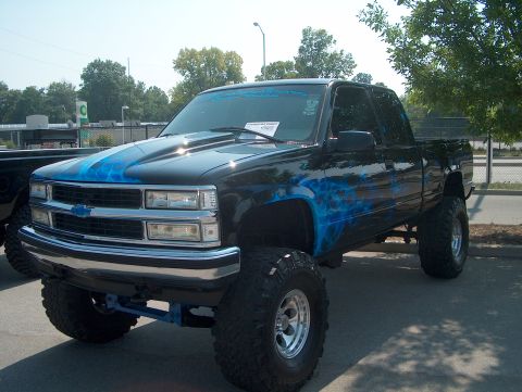 1978 Ford Bronco - A modified black pickup truck is parked outdoors, custom blue flame paint and a lifted suspension.