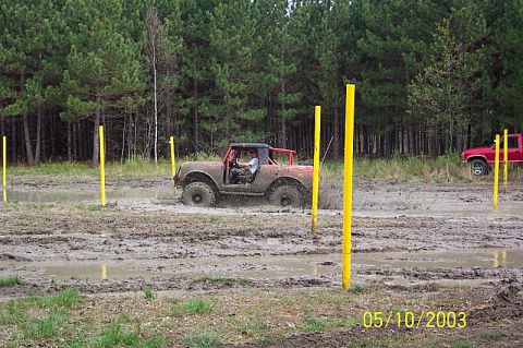 1978 Ford Bronco - A 1978 Ford Bronco navigates a muddy obstacle course, with another red vehicle visible in the background.