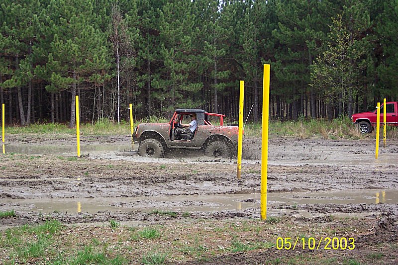 Brown 1978 Ford Bronco driving through mud obstacle course with yellow poles