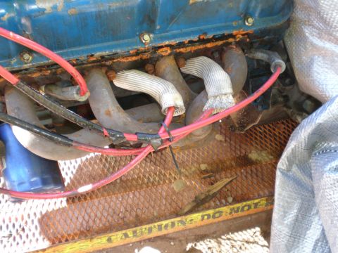 1966 Ford Mustang - Close-up view of an engine blue valve covers and red spark plug wires, with exhaust manifolds and caution tape in the background.