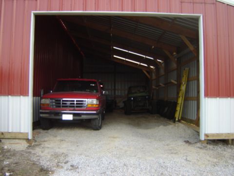 1992 Ford Bronco - A red pickup truck is parked inside a barn, with another vehicle chassis visible in the background.